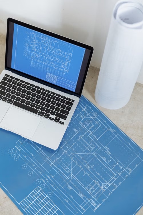 Laptop and technical blueprints representing drawing control in manufacturing