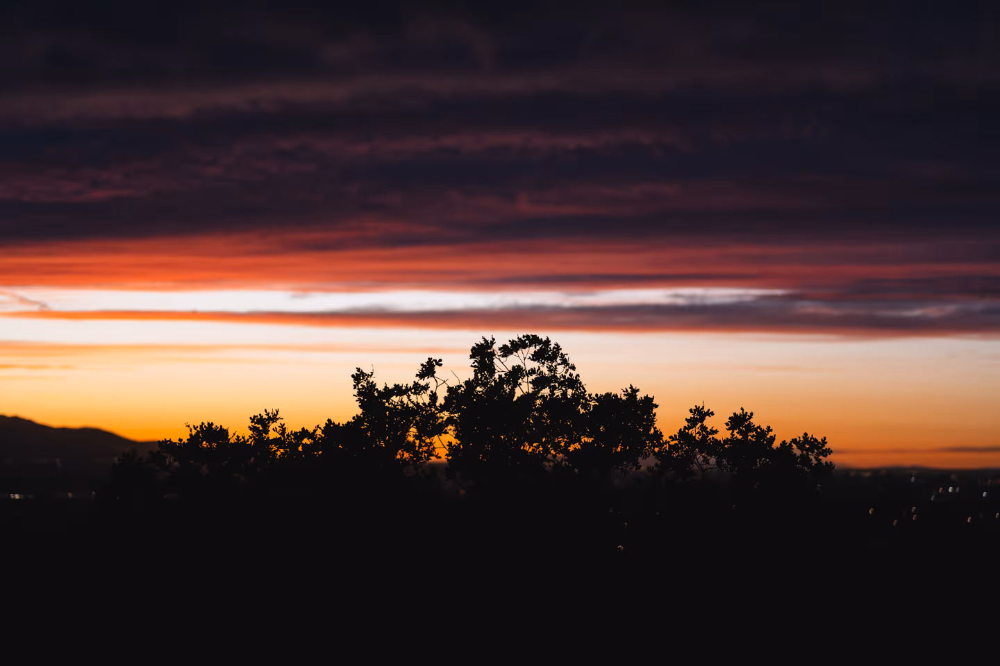 A vivid sunset over a darkened landscape with deep purple and red clouds streaking the horizon.
