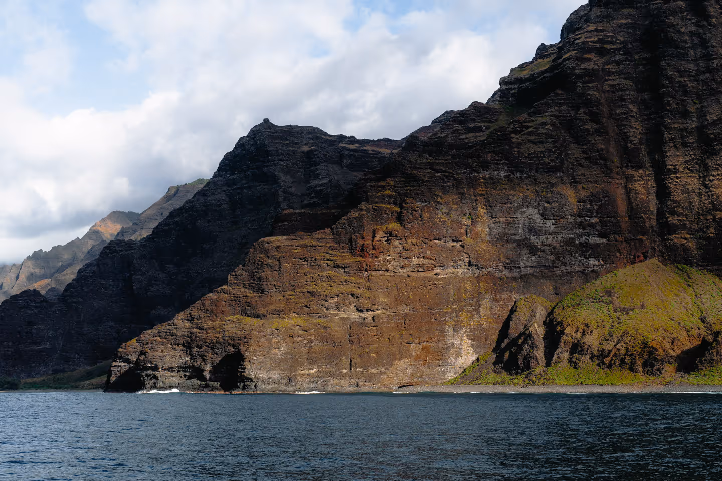 Rugged seaside cliffs rising from deep blue ocean water with patches of greenery near the shore.