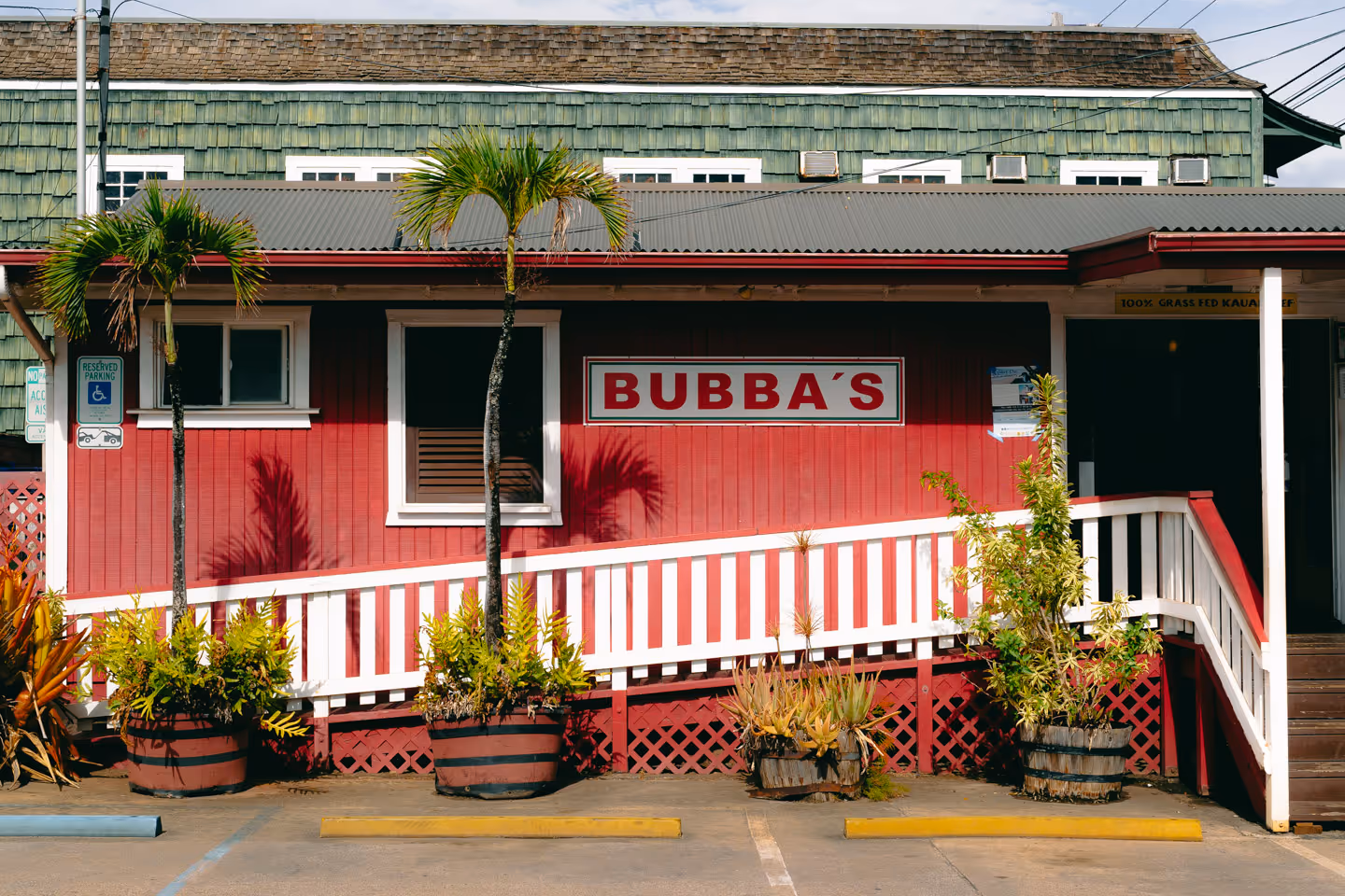 A red and white restaurant building with a sign reading “Bubba’s,” surrounded by potted plants and palm trees.