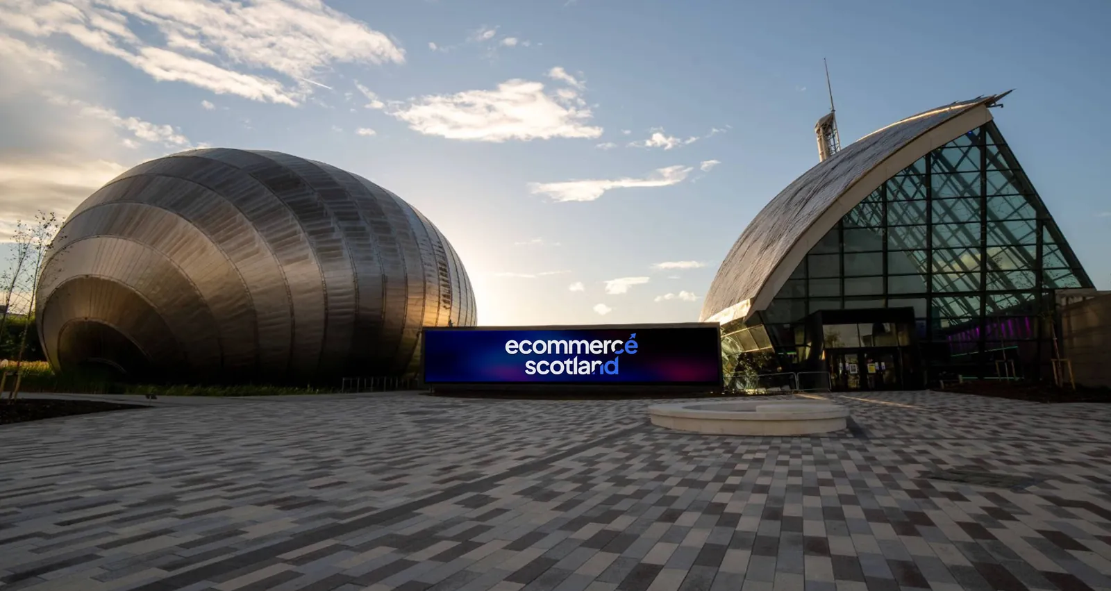 The IMAX cinema and Glasgow Science Centre at sunset, with an Ecommerce Scotland screen between them