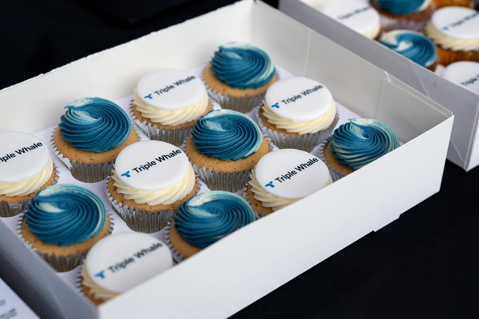 A box of cupcakes topped with Triple Whale logo discs and blue icing