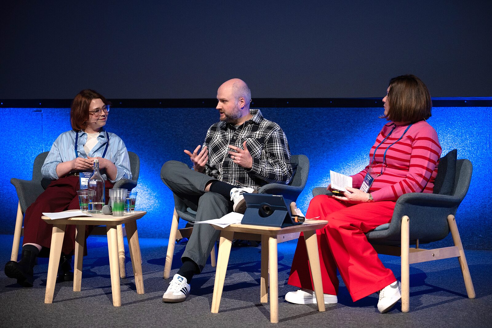 Three panellists in armchairs on the blue-lit IMAX stage, the man in the middle gesturing as he speaks