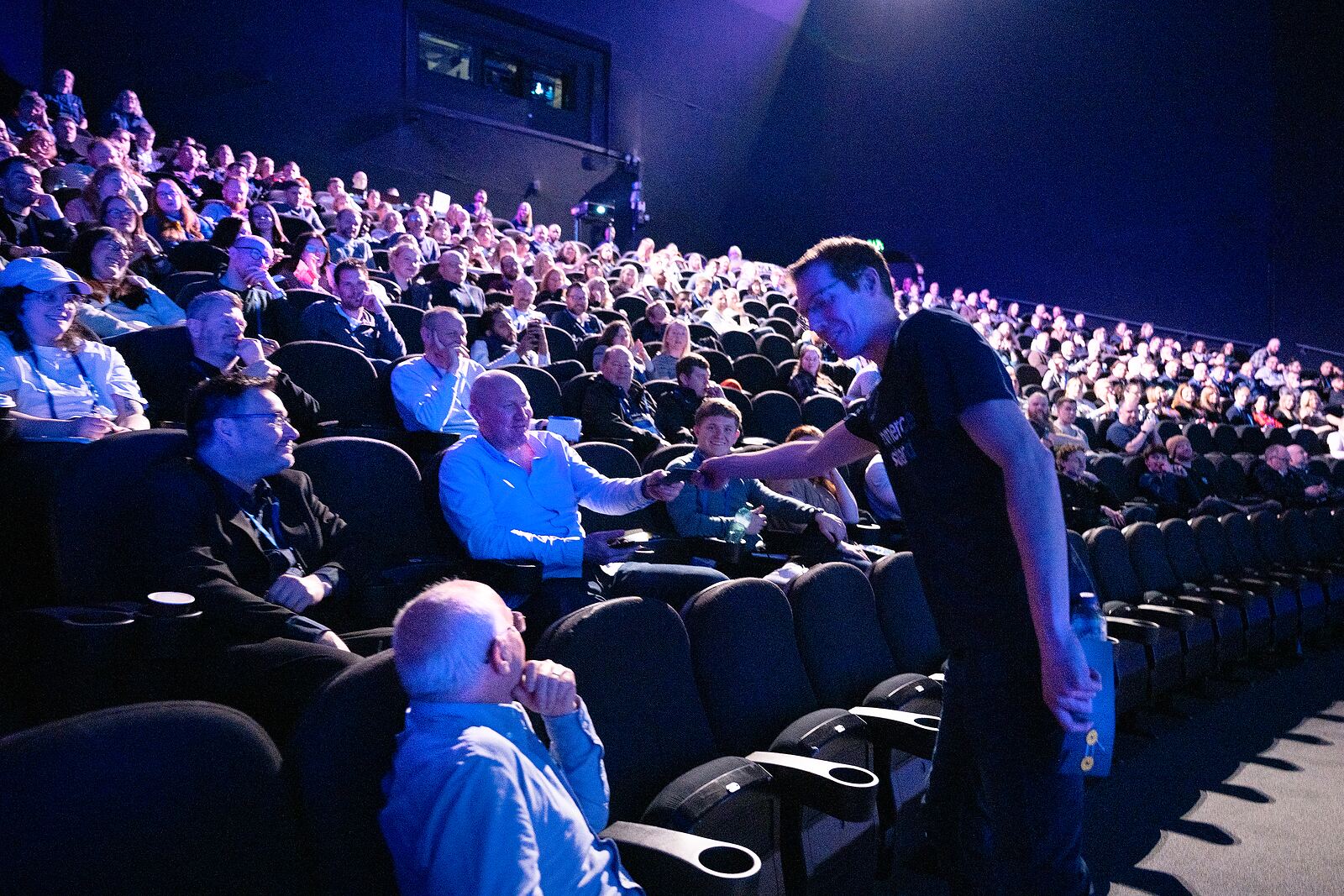 A packed, brightly lit IMAX auditorium as a microphone is passed to an attendee