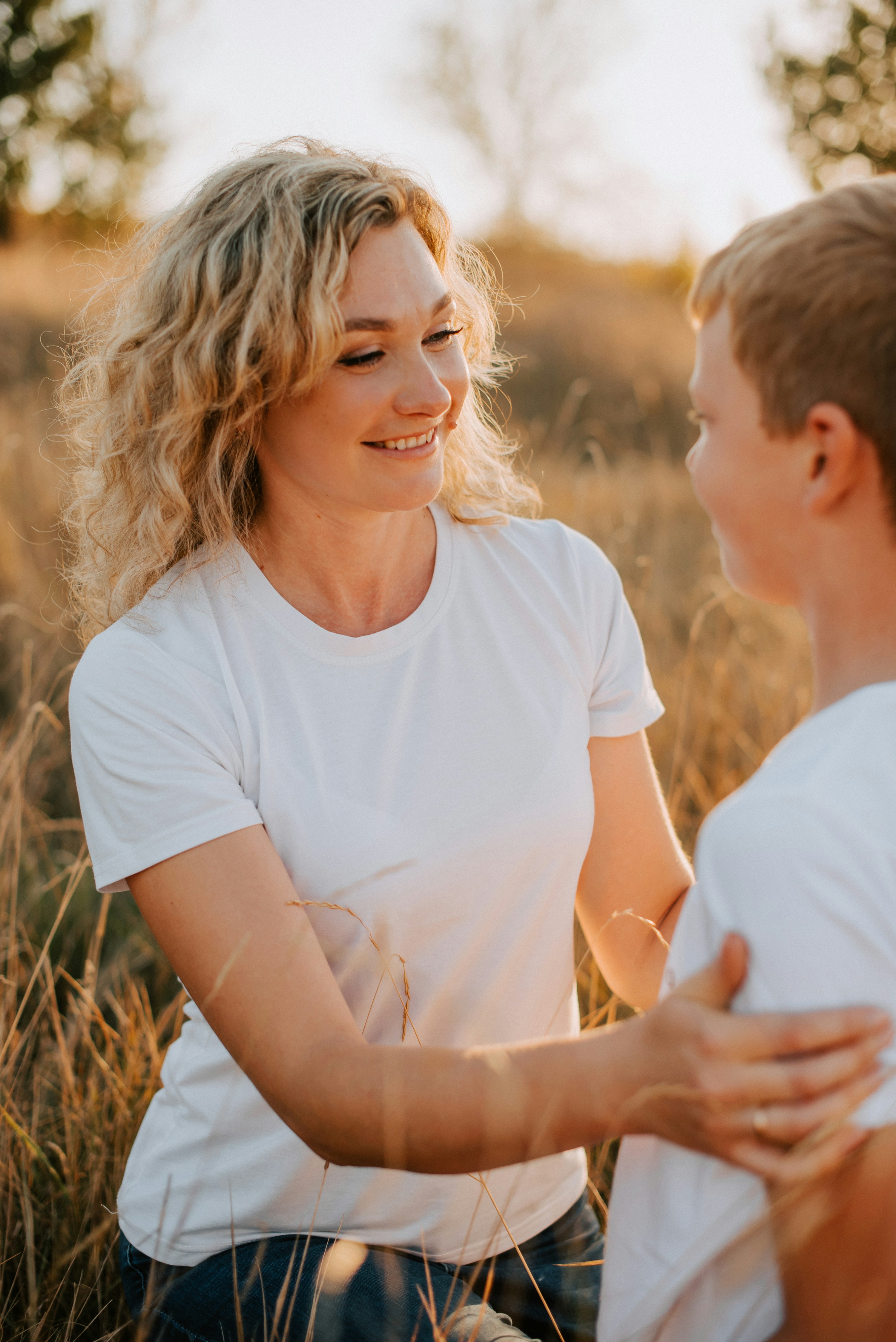 Mother smiling and talking with her teenage son outdoors, her hands on his arms in support.