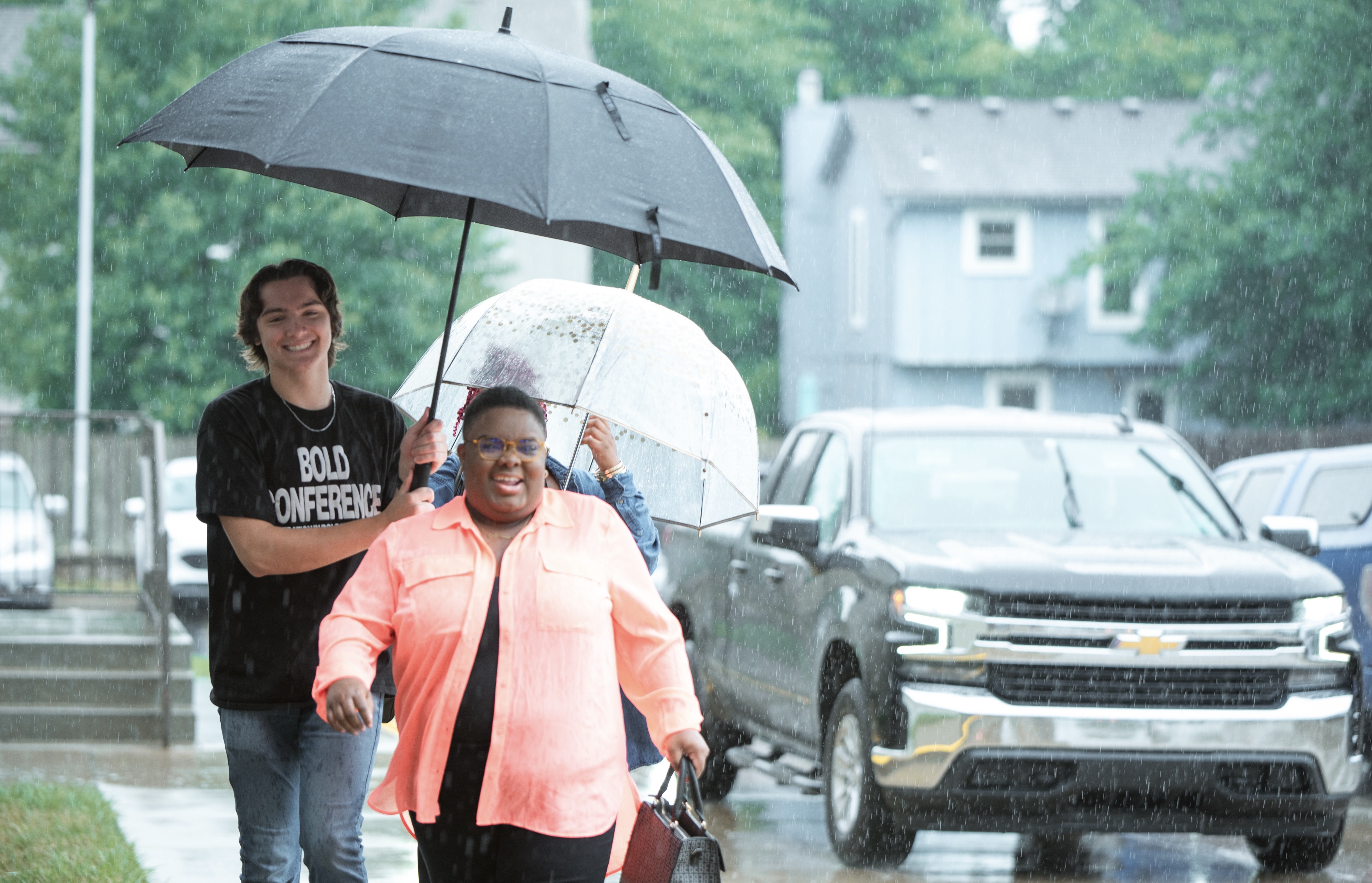 A young church volunteer escorts a church member to the church in the rain, he holds an umbrella over her head to protect her from the rain