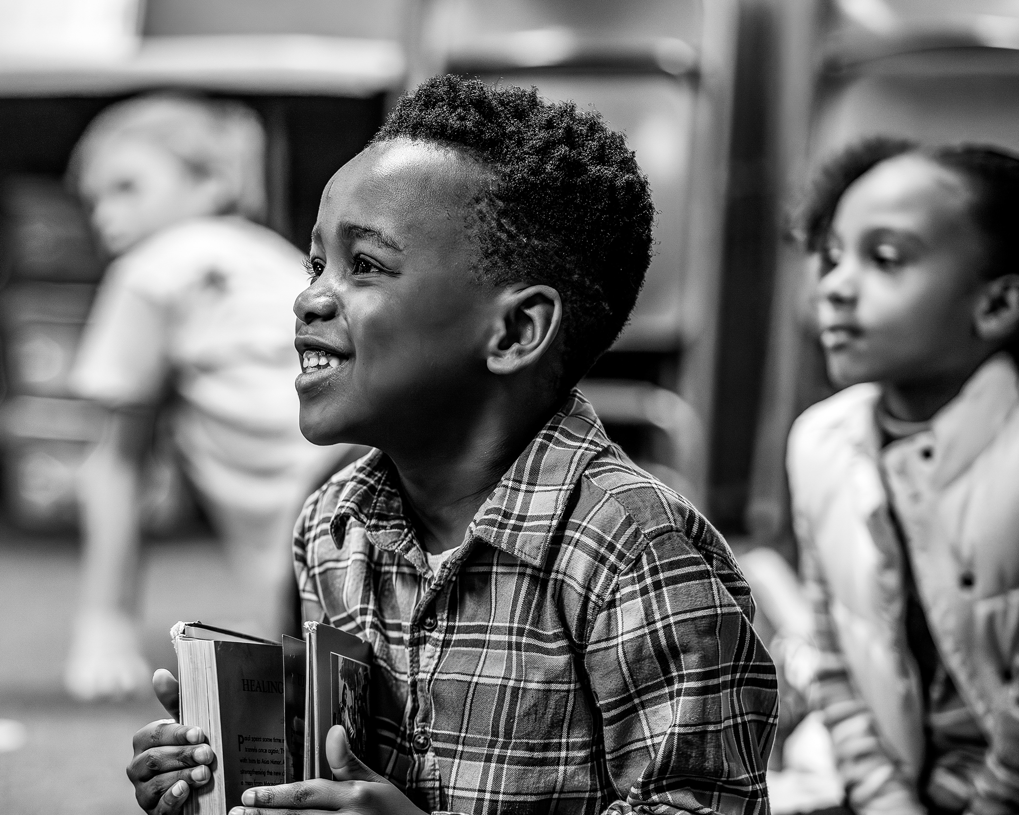 Young boy in plaid smiling with his Bible as he sits through a Harvest Kids lesson. 