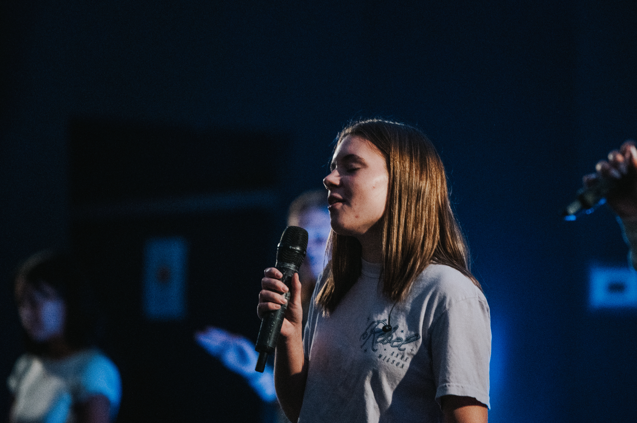 A young woman sings into the mic, her eyes closed, smiling as she sings. 