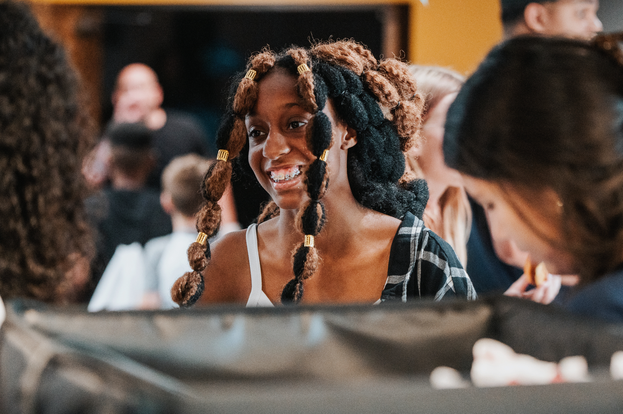 A young woman with a beautiful black and light brown weave smiles at her friends