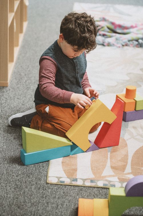 A little boy playing with colored blocks in various geometric sizes