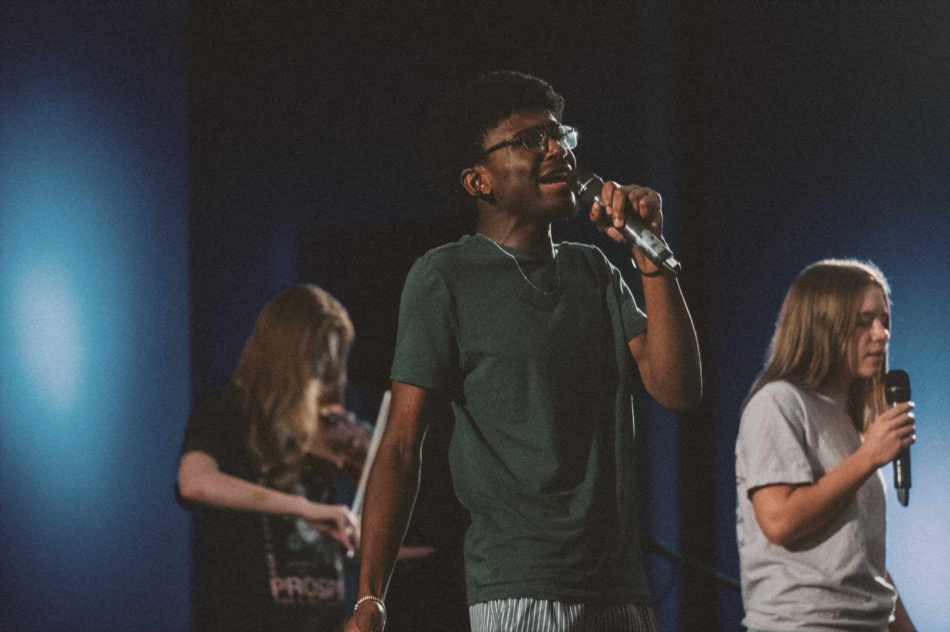A young man and two young women lead worship for the Harvest Youth. 