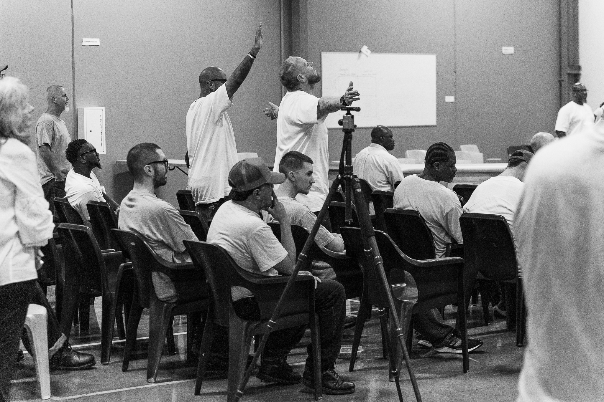 A black and white image of a group of men in prison raising their arms in worship