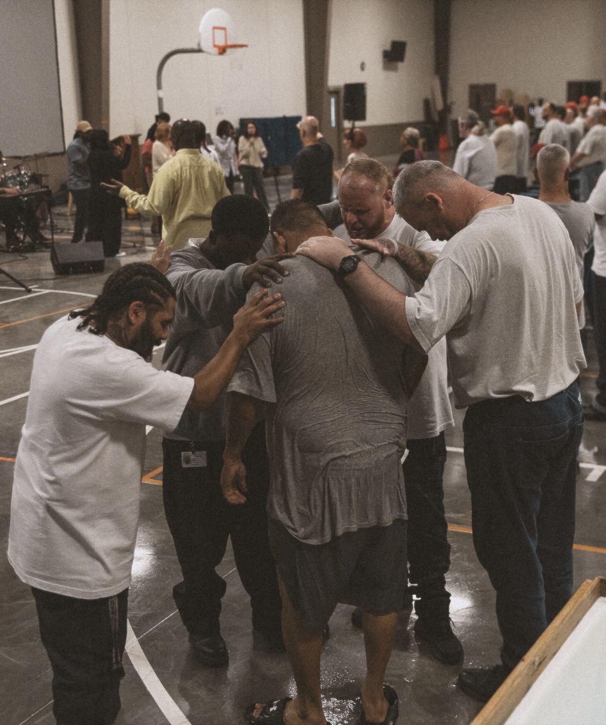 A group of men huddled around another man in prayer at the prison outreach