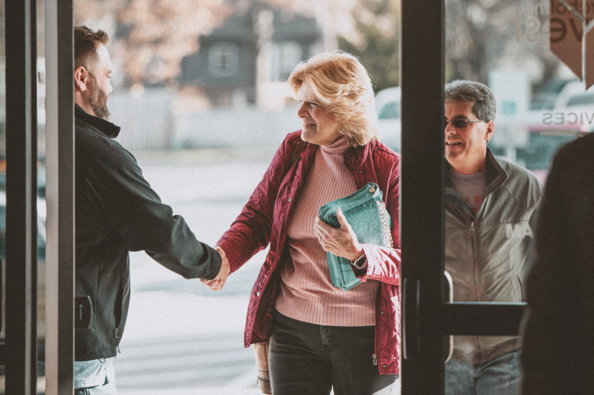 Blonde woman being greeted at the door of Church of the Harvest by a door greeter. 