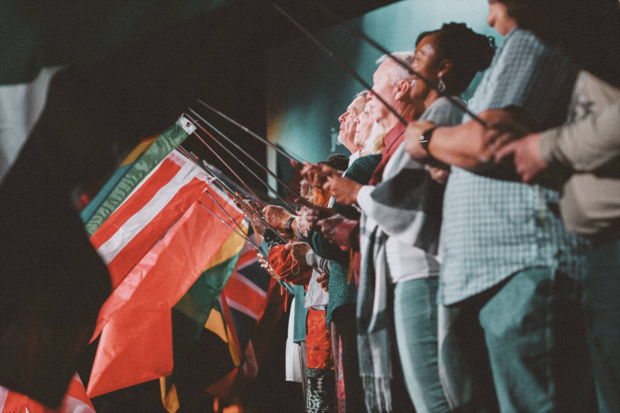 A row of Church of the Harvest members holding their native country flag on stage, The image represents the diversity of the congregation at Church of the Harvest.