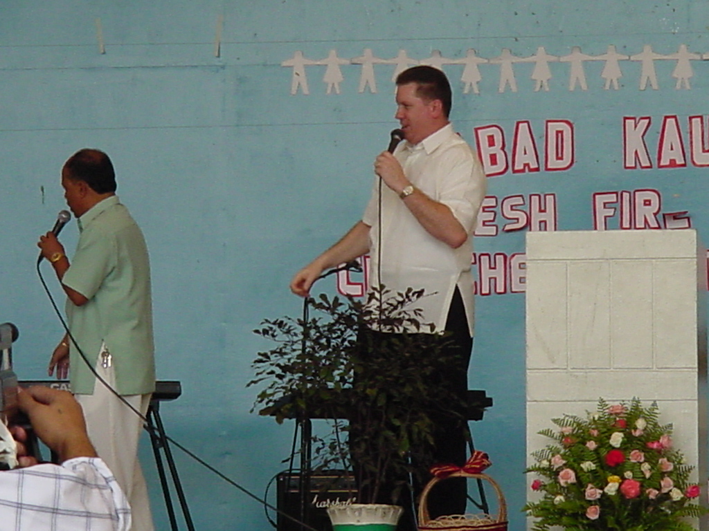 Pastor David preaching in the Philippines with a blue wall and red lettered banner behind him