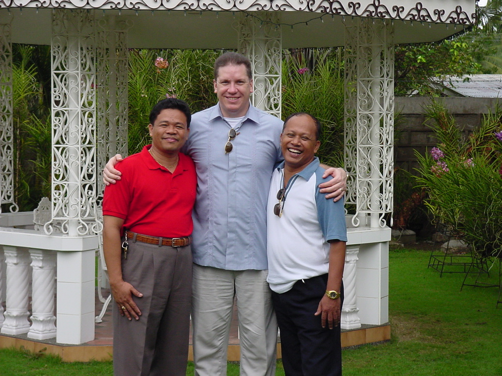 Pastor David, Tony and Ernie pose for a cheerful photo outdoors in a garden area, standing in front of a gazebo.