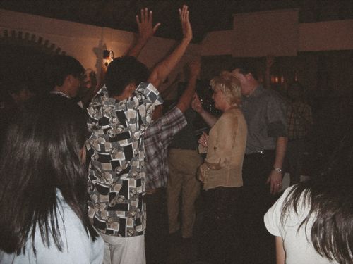Pastors David and Tracy minister to attendees as several people raise their hands during a lively indoor worship gathering.