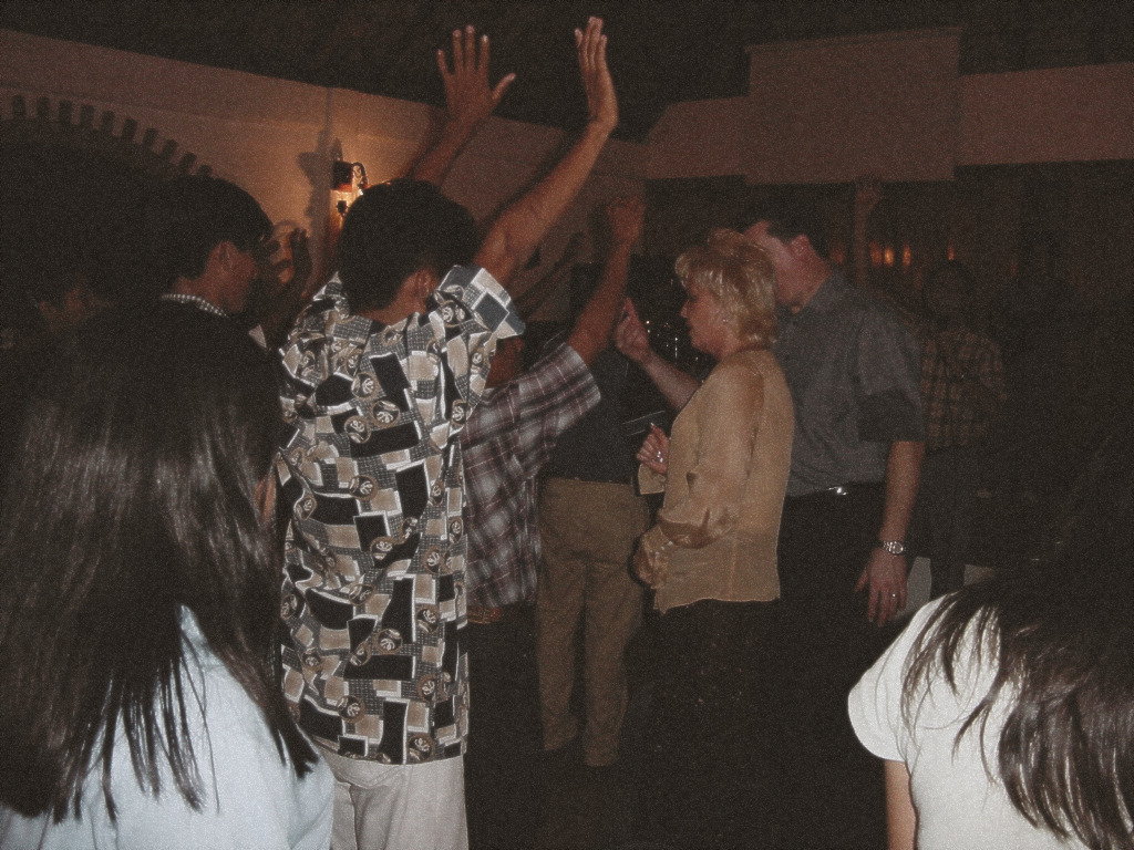 Pastors David and Tracy minister to attendees as several people raise their hands during a lively indoor worship gathering.