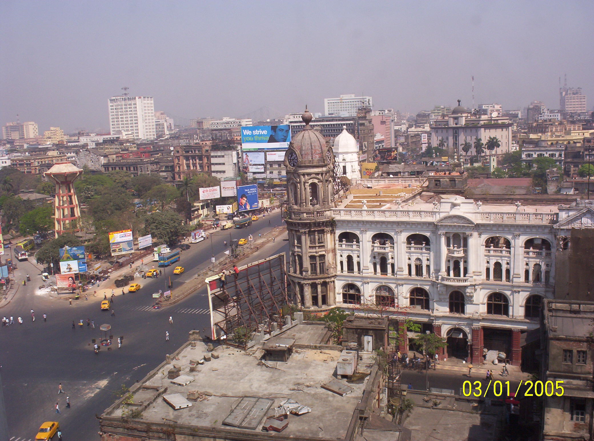 A cityscape showing a large intersection with vintage architecture, billboards, and yellow taxis moving through the streets on a hazy day.