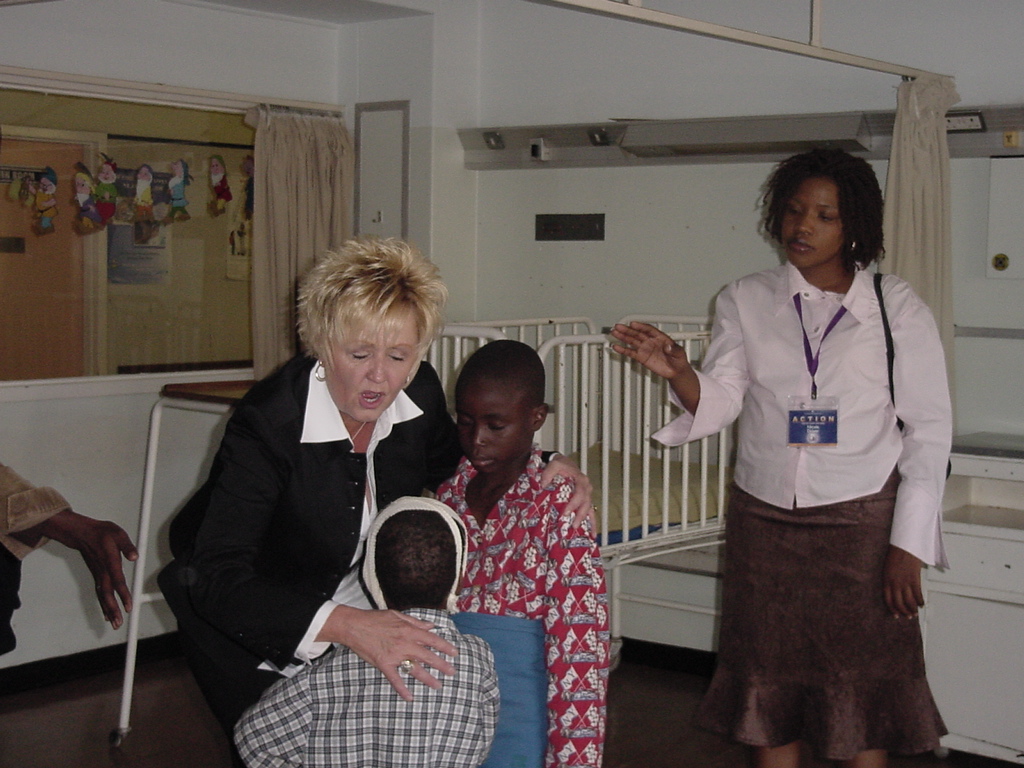 Pastor Tracy prays with two children, one wearing a head bandage, as another woman extends her hand in prayer.