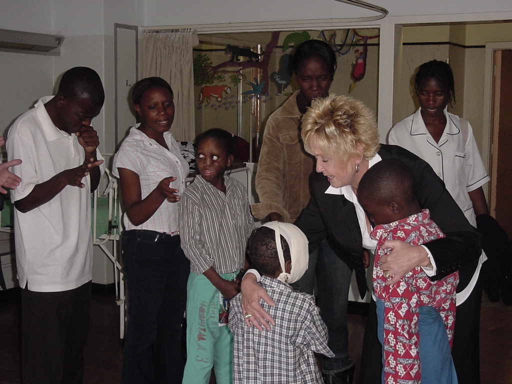 Pastor Tracy embraces and prays for two children in a hospital room while nurses and others observe.