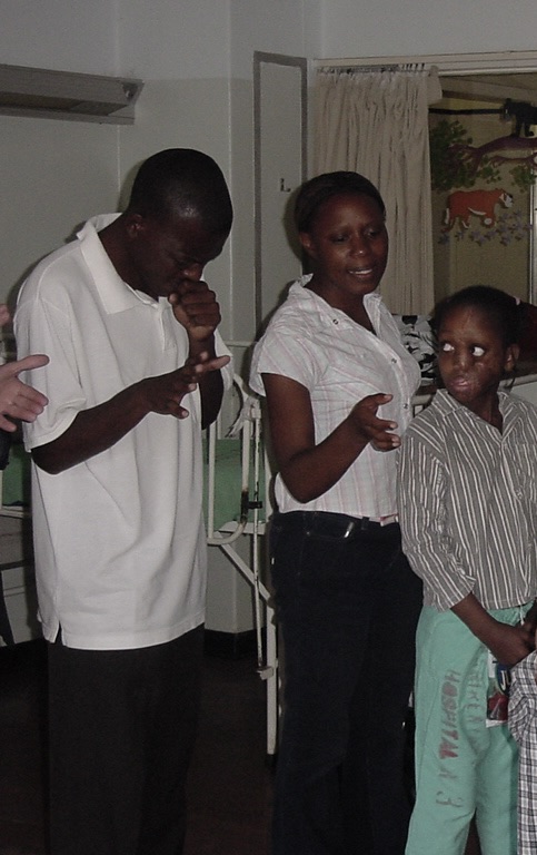 A young family stands by and watches as Pastor Tracy prays over the little children. 