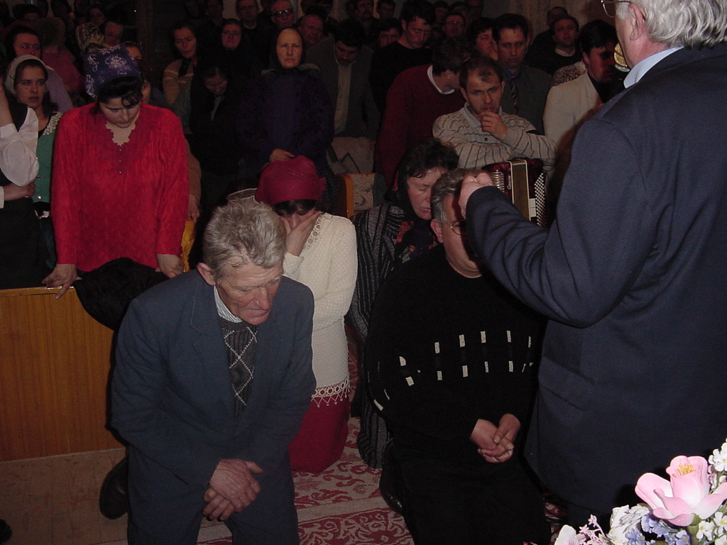 A congregation kneels and bows their heads in prayer during an altar call inside a Romanian church.