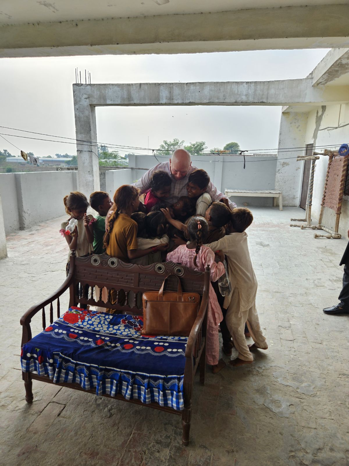 A group of children gather in a joyful hug around Pastor David inside a partially constructed building.
