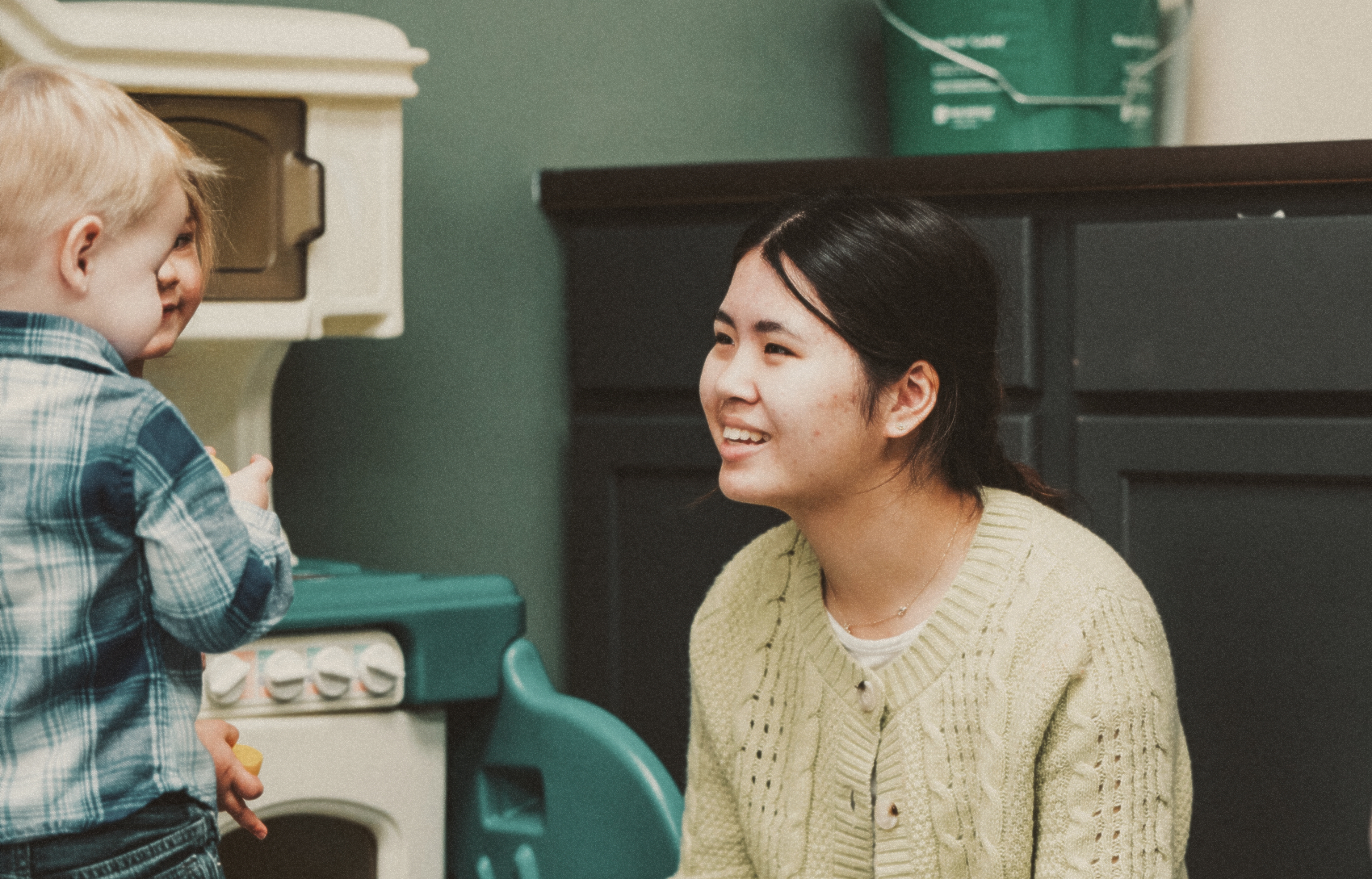 A young woman volunteering in Harvest Kids, smiles as she interacts with two young children. 