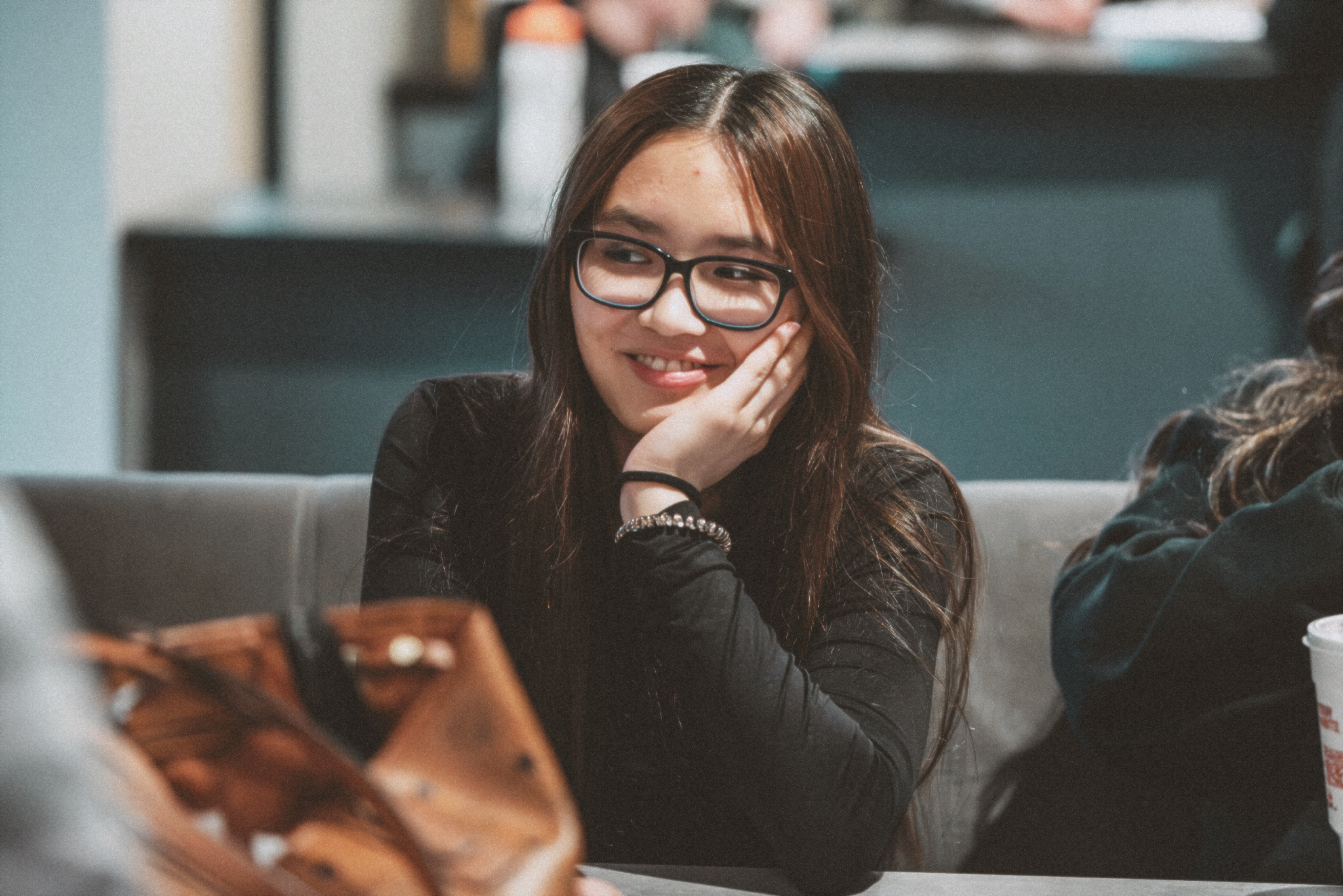 A young woman with glasses smiles and rests her face in her hand as she takes in the lesson. 