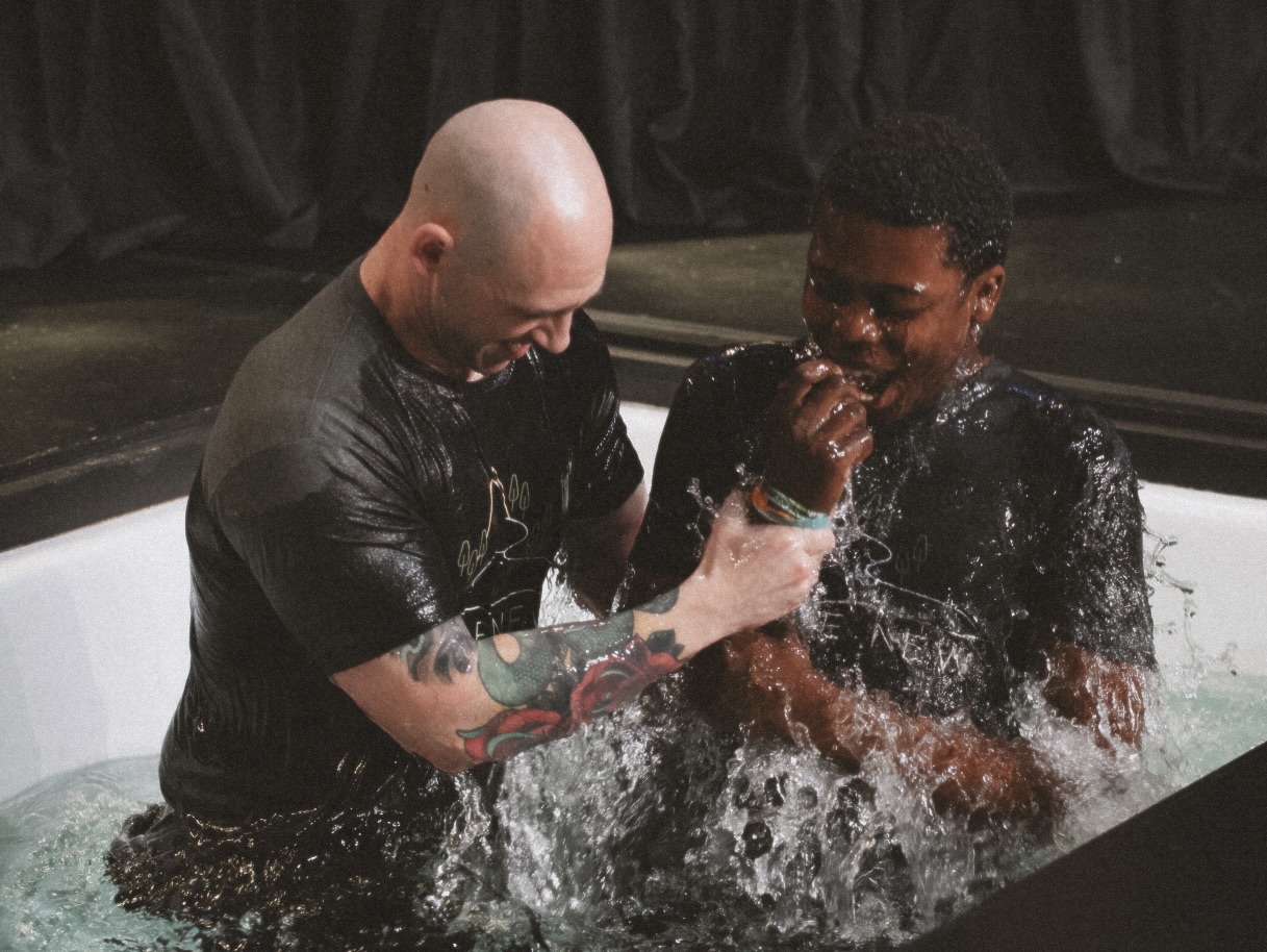 Pastor Royce and young man in baptism tank. Pastor Royce grips young mans wrist as he brings the young man up out of the water. The young man smiles in joy.