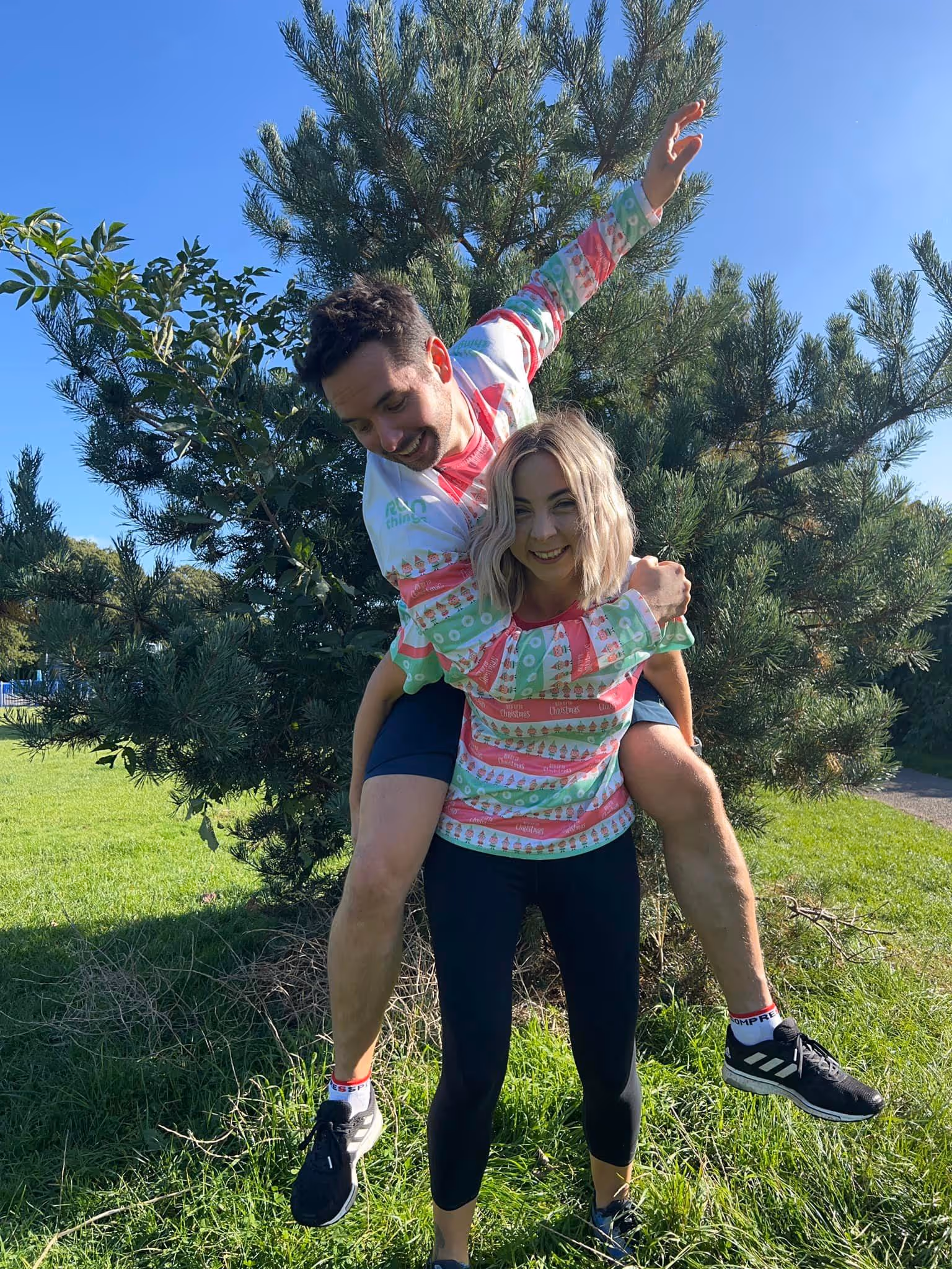 Two models wearing the run things christmas kit. The female is giving the male a piggy back.