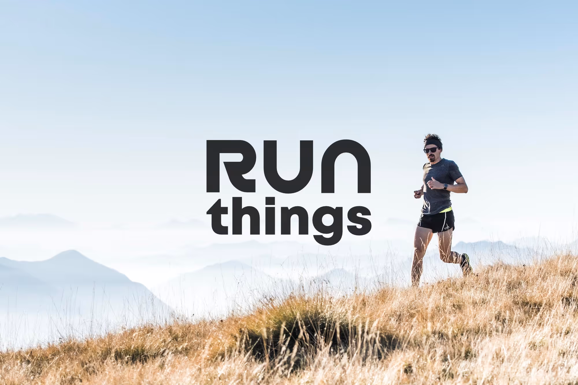 A runner crossing a grassy tussock with mountains in the backdrop. The run things logo takes centre stage in the middle of the image