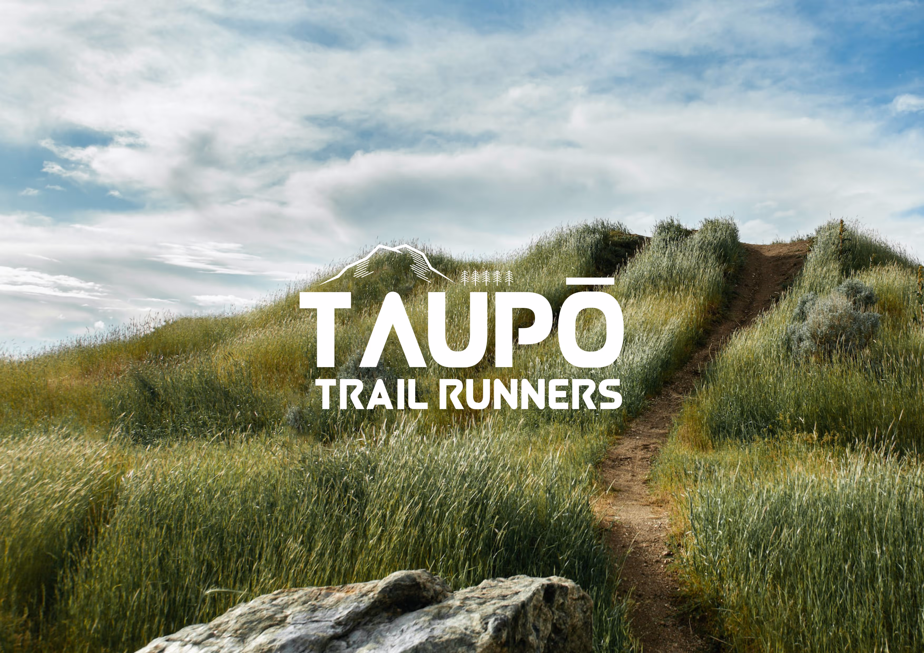 A grassy hill running off into the distance with the Taupo Trail Runners logo in the middle