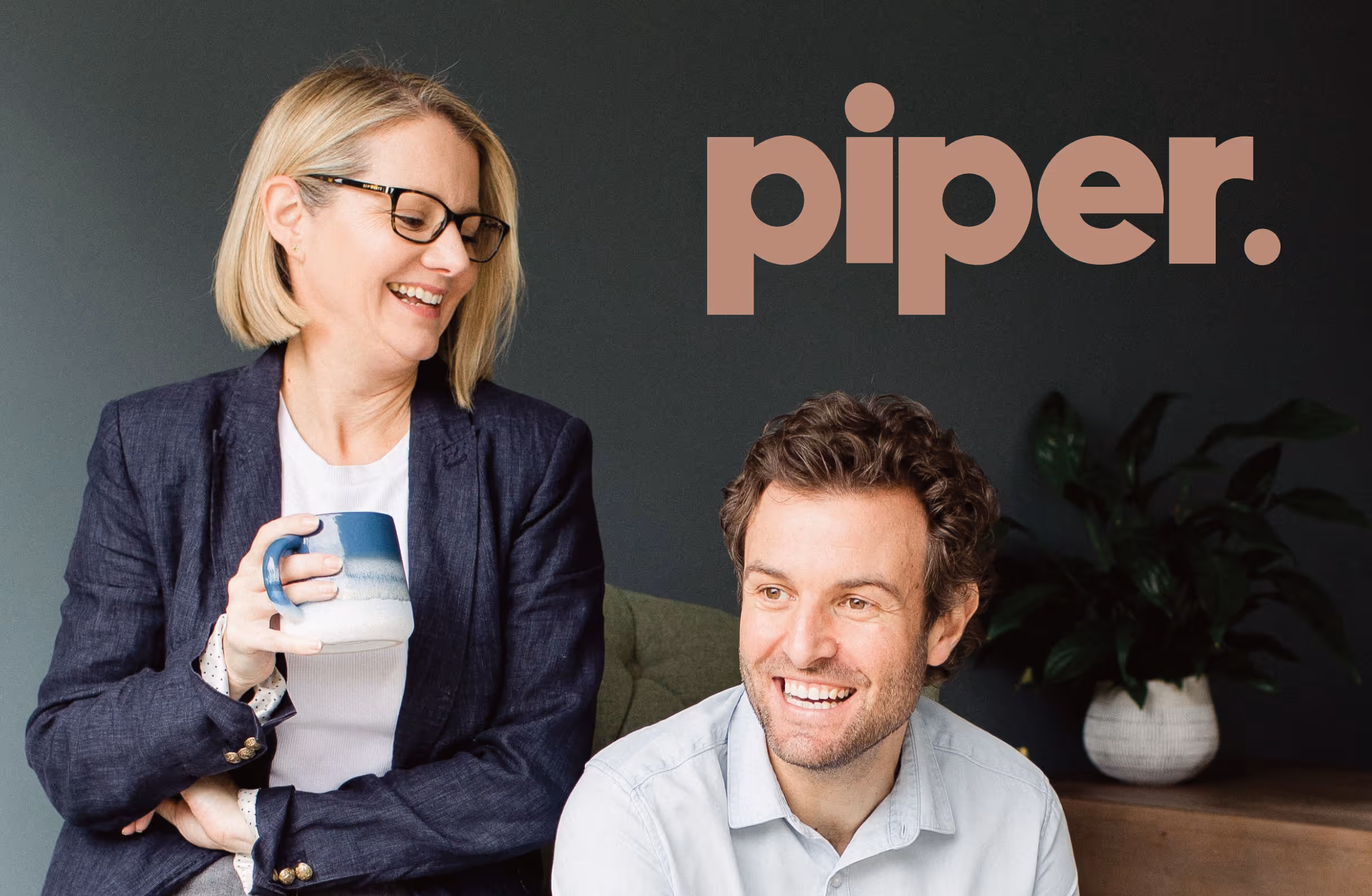 An adult couple look relaxed and smile in a living room setting with the piper logo in brown sitting top right of the photo.