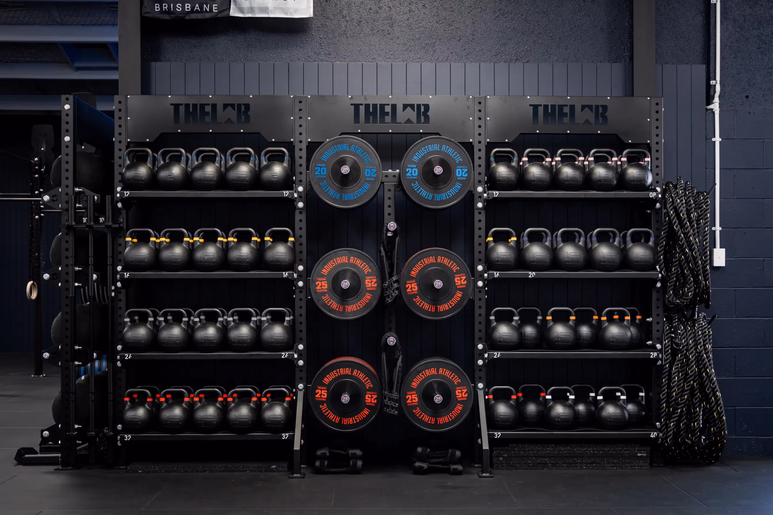 A large, setup with multiple rows of weights on a rack. Situated in a dark, industrial looking gym environment