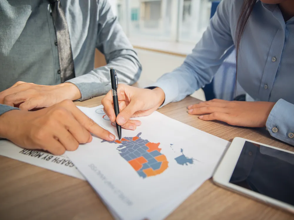 Two colleagues marking target markets on a printed map report