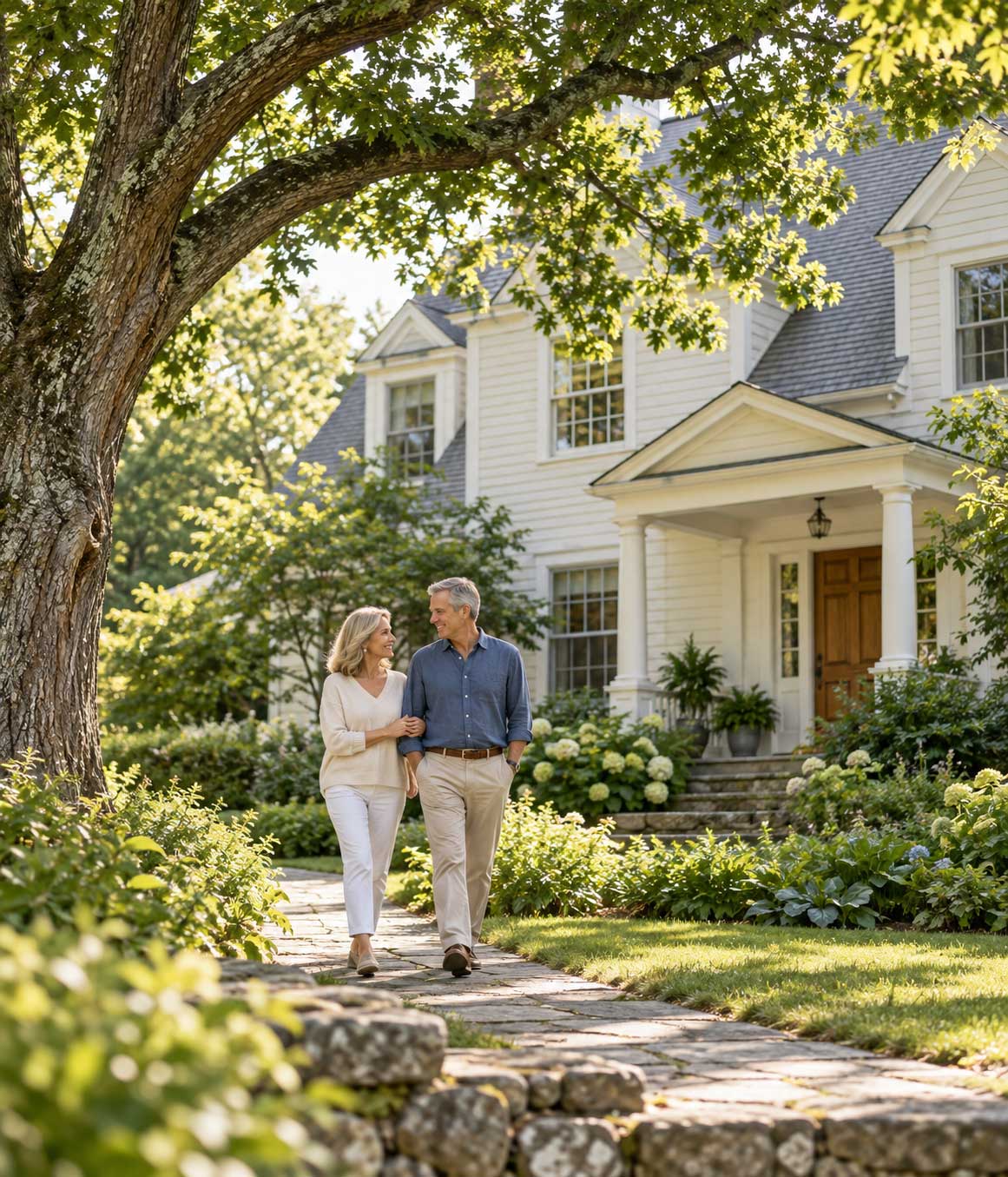 A couple beside a mature tree and a Connecticut-style home