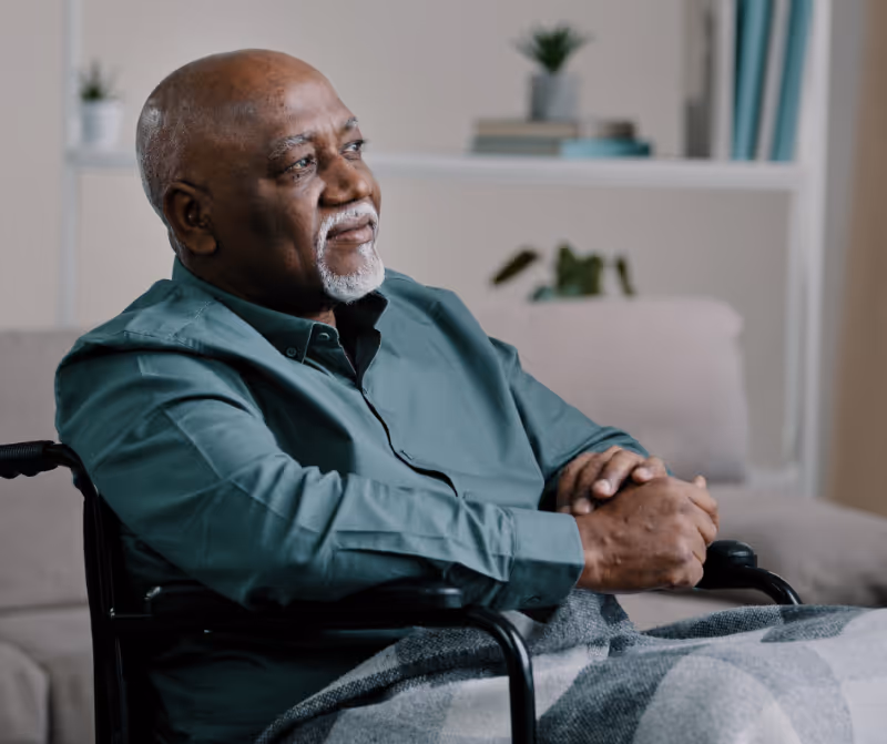 Elderly man sitting at home with a caregiver offering support, symbolizing aging, independence, and assisted living needs. Milford elder law 