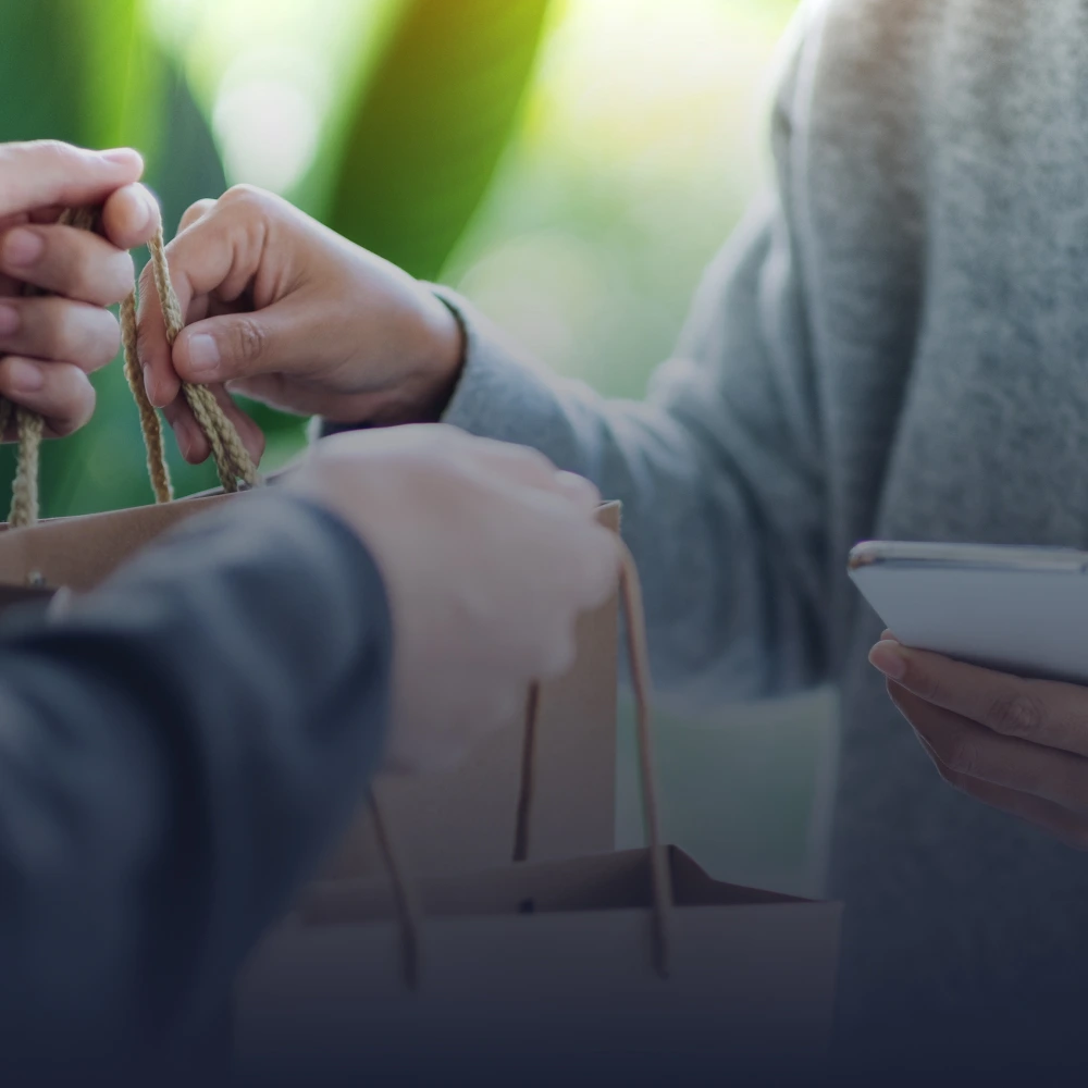 Hands exchanging shopping bags and the customer doing a search on their phone.