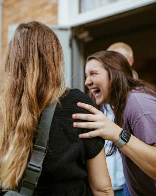Young woman warmly greeting and embracing another person.