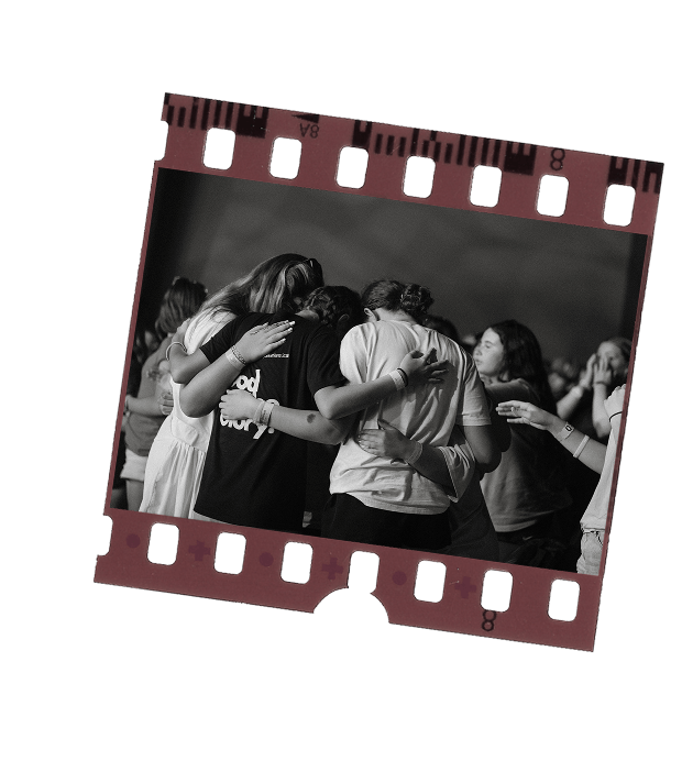 Black and white photo of an enthusiastic crowd at a concert with hands raised and stage lights overhead.