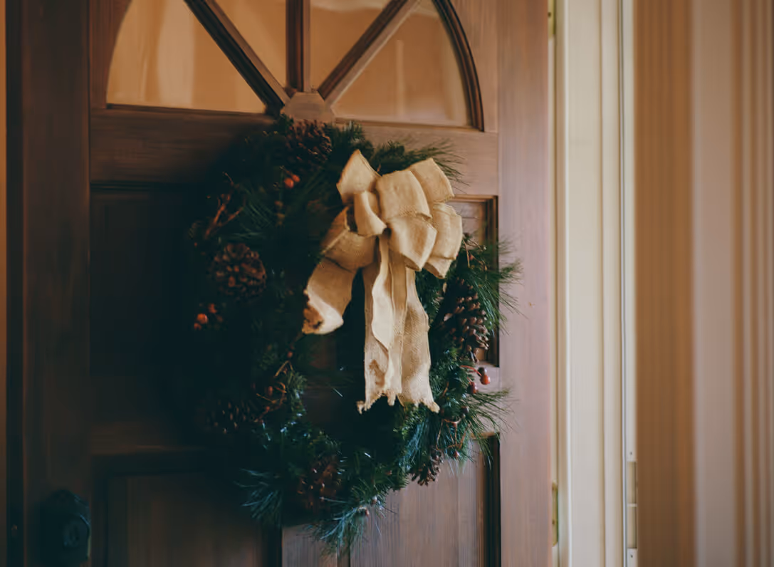 Christmas wreath with pinecones and a large burlap bow hanging on a wooden door.