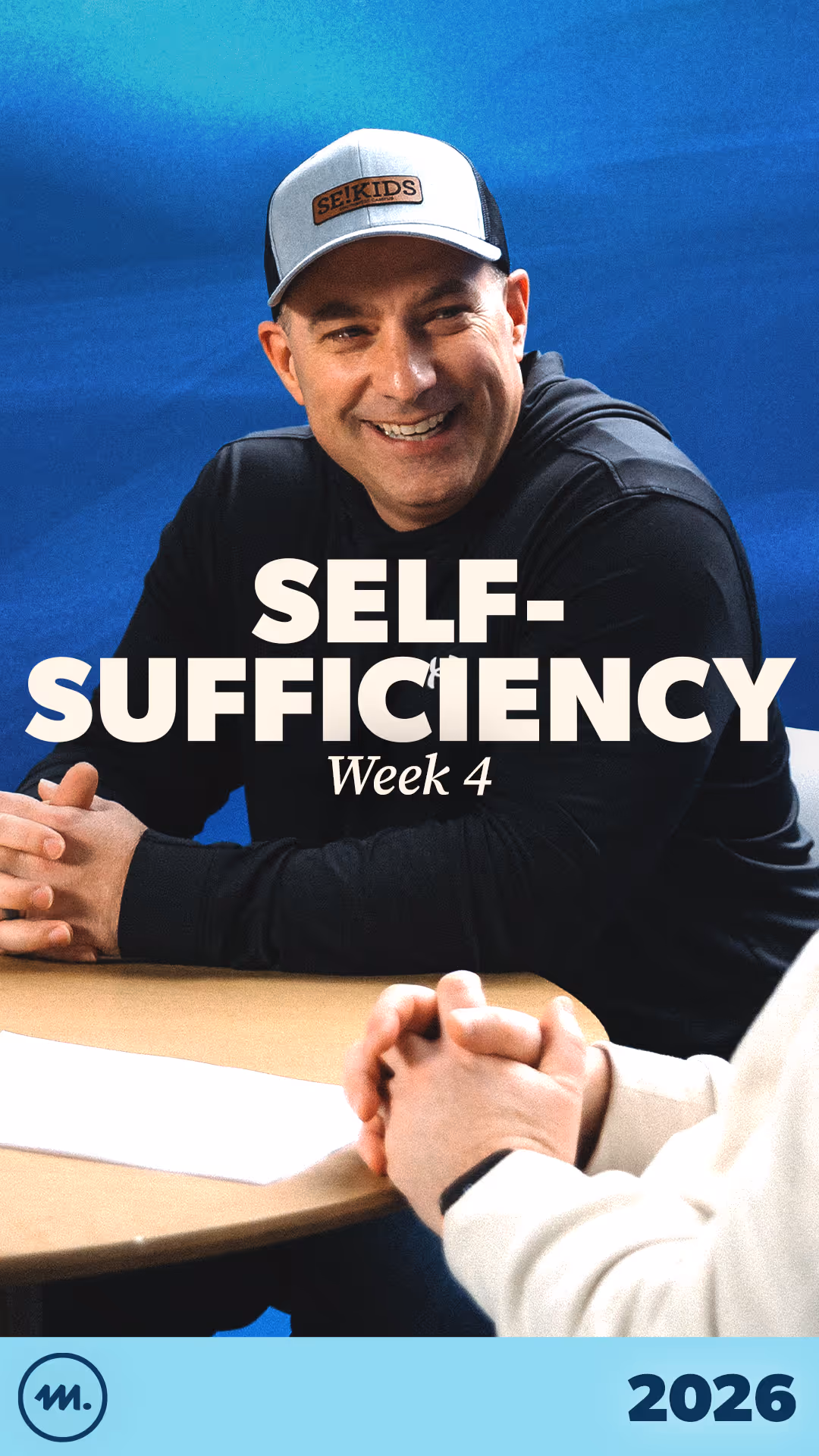 Smiling man in a baseball cap and black shirt sitting at a table with folded hands, with text 'SELF-SUFFICIENCY Week 4' overlaid.