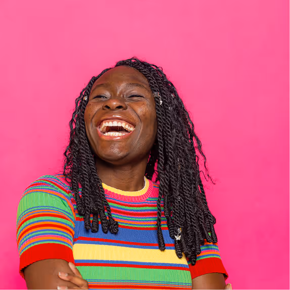 Smiling woman with braided hair wearing a colorful striped shirt against a bright pink background.