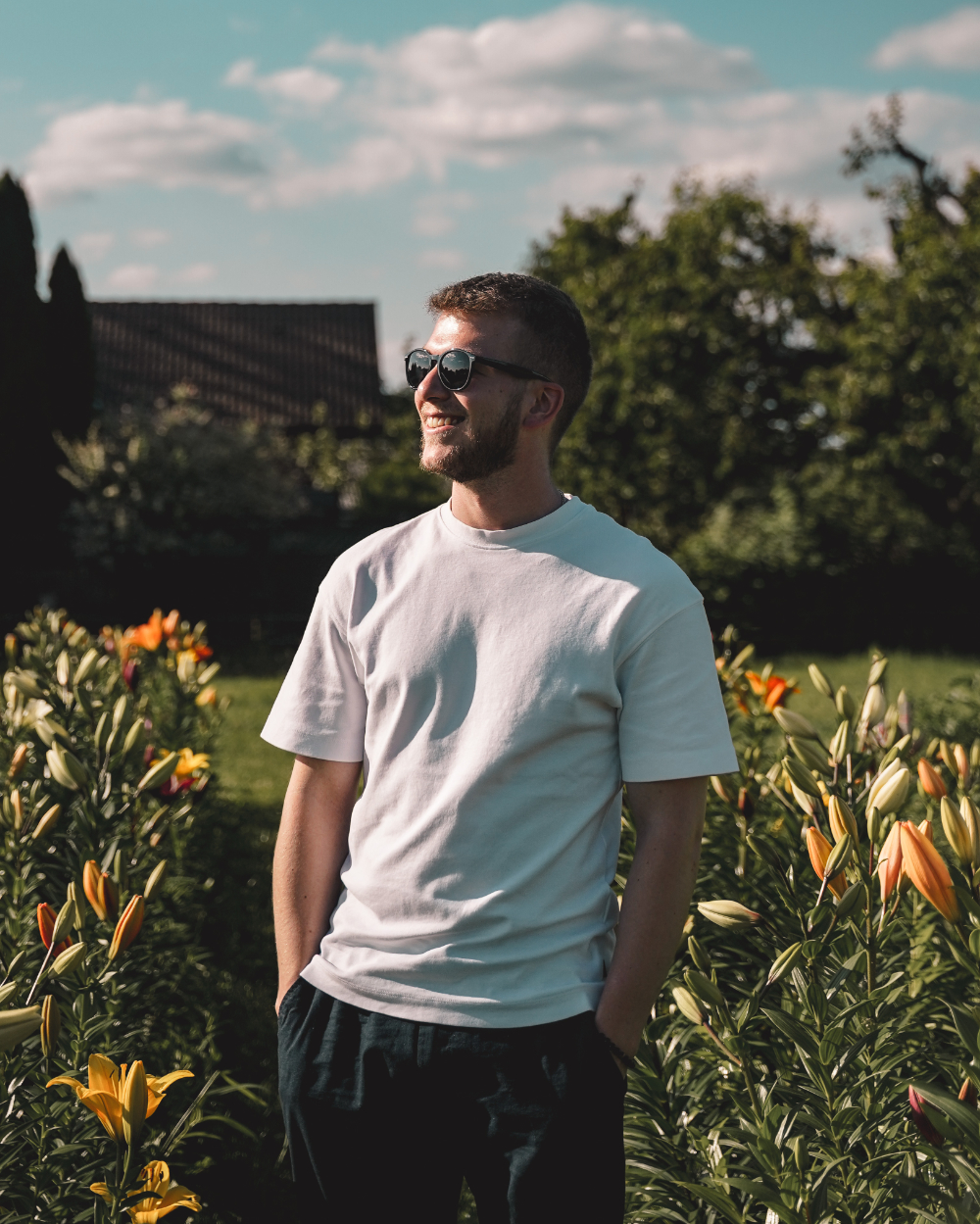 Selbstporträt von Dominic, dem Fotografen von Dommeshots, der in einem Bunten Blumenfeld steht und zur Sonneschaut