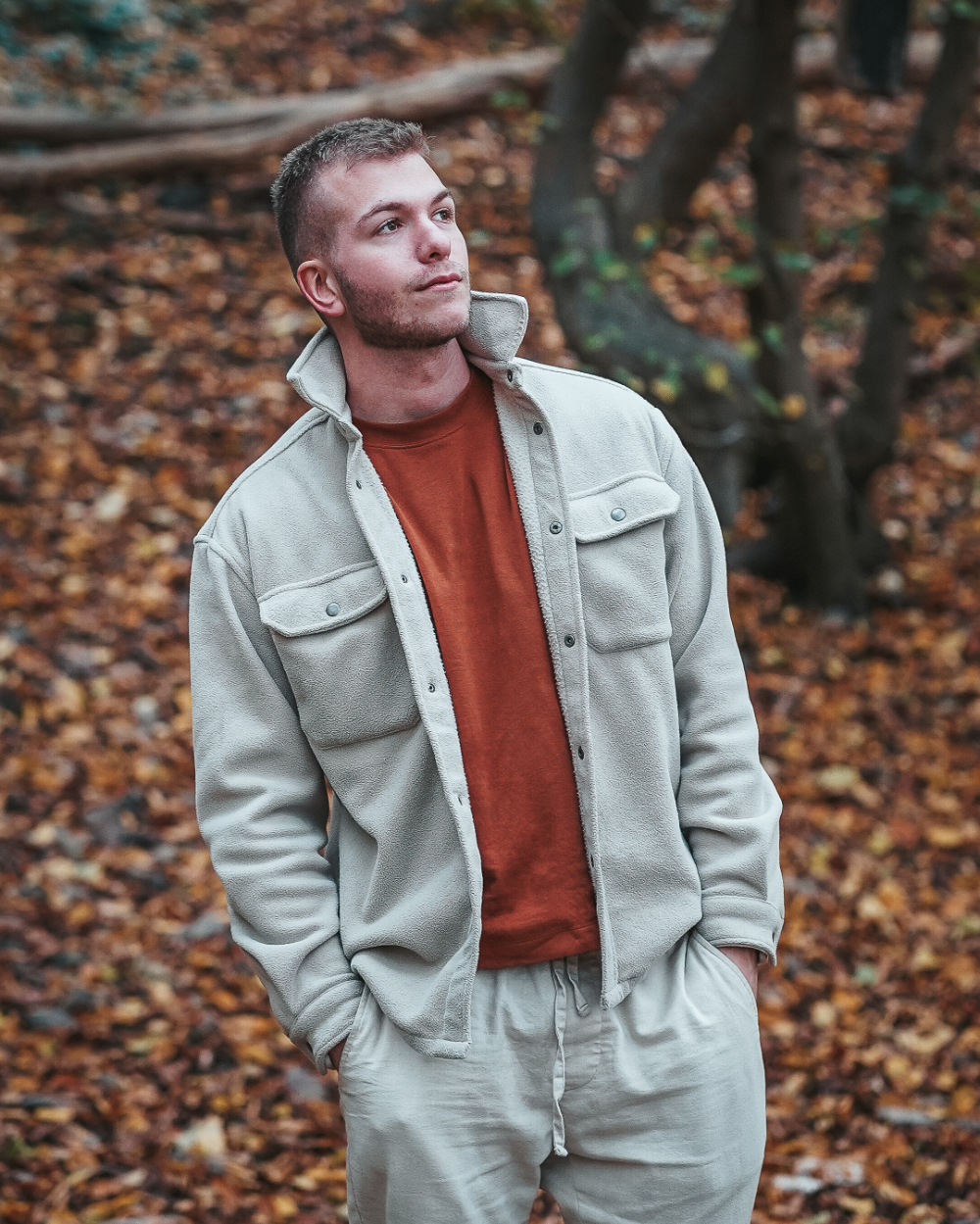 Porträt von Dominic Freigeber, dem Fotografen hinter Dommeshots, im Wald. Mit beiger Jacke und Hose schaut er Richtung Sonne