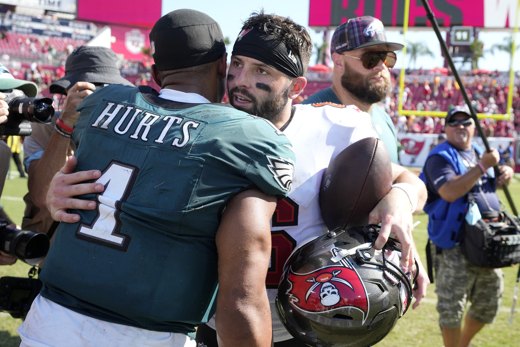 QBs Baker Mayfield and Jalen Hurts hug at an NFL game.
