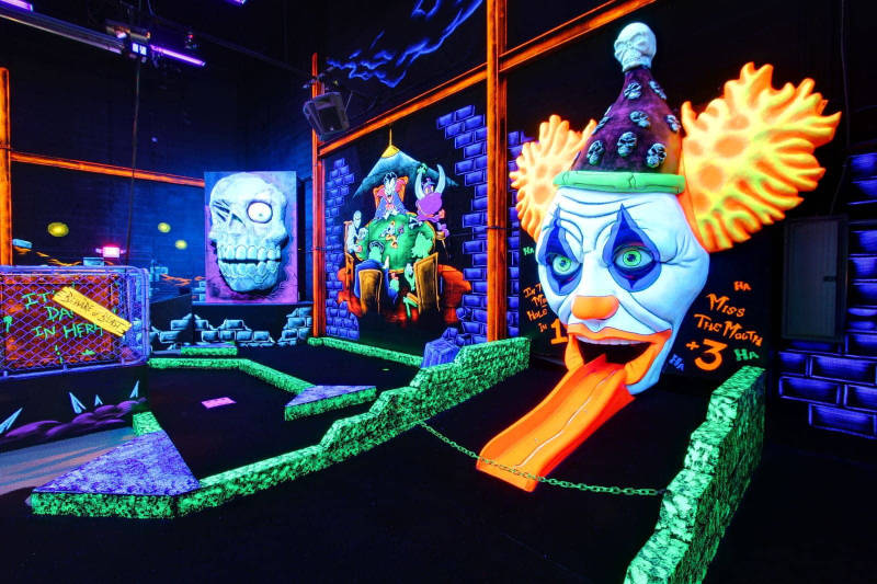 Interior mini golf course with bright neon lights in dark room.